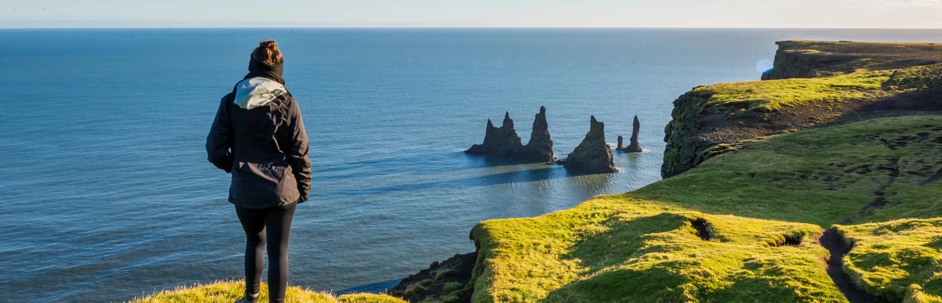 En person på Dyrhólaey med udsigt over Reynisdrangar og Atlanterhavet.
