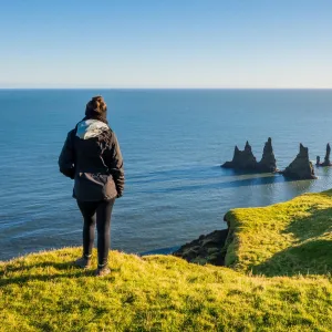 En person på Dyrhólaey med udsigt over Reynisdrangar og Atlanterhavet.